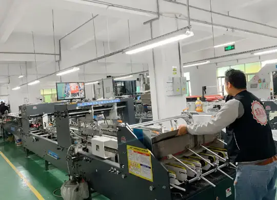 Factory worker operating an automatic folder gluer machine for custom chocolate folding boxes and paperboard packaging production
