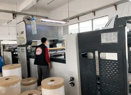 Factory worker operating an automatic laminating machine for custom chocolate packaging boxes and printed paperboard packaging production