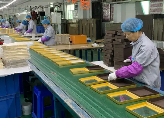 Workers assembling custom chocolate gift boxes by hand on a factory production line for premium paperboard packaging