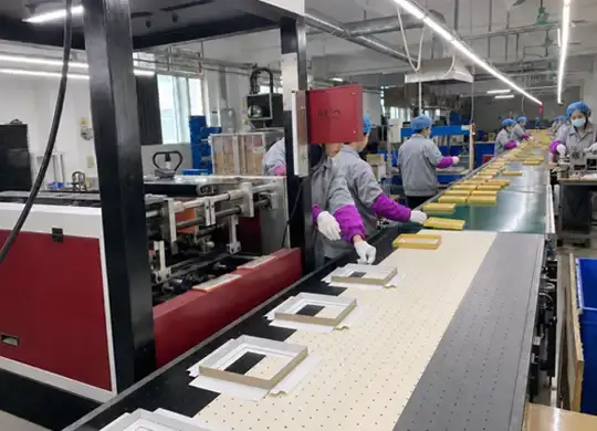 Workers assembling custom chocolate gift boxes on a factory production line with semi-automatic equipment for premium paperboard packaging